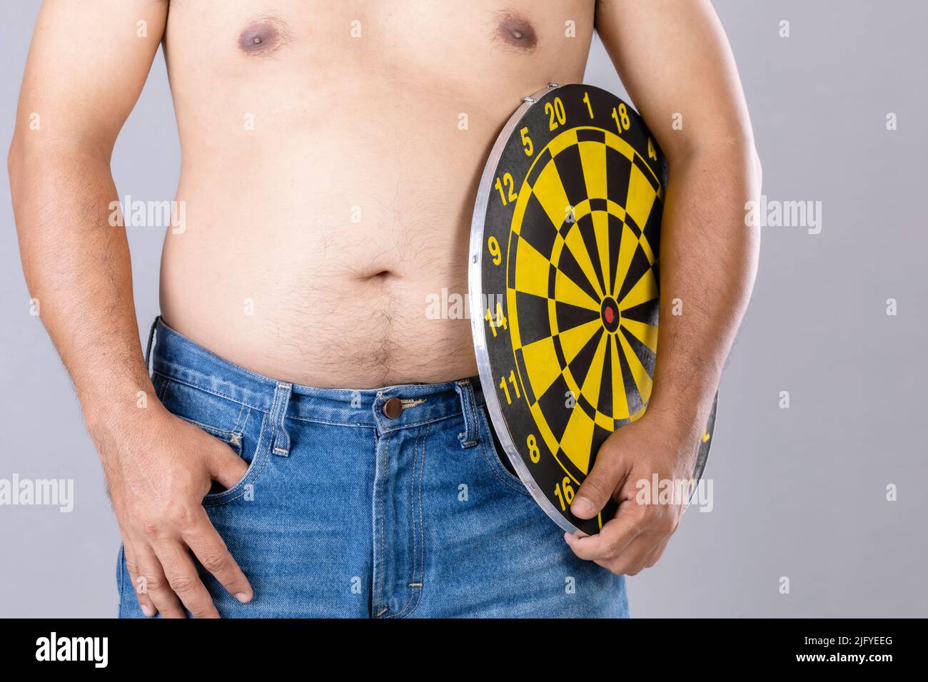 Fat Menschen halten rund gelbe Dartscheibe neben seinem Bauch Position. Ziel der Gewichtsverlust Konzept. Studioaufnahme isoliert auf grauem Hintergrund Stockfoto