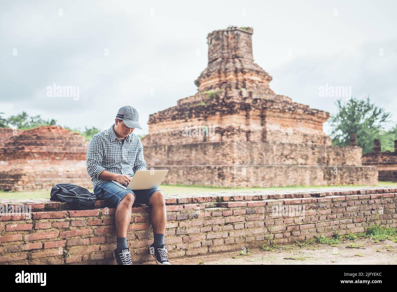 Asiatischer Tourist, der im Sukhothai Historical Park, Thailand, arbeitet und einen Laptop benutzt. Urlaubs- und Urlaubskonzept Stockfoto