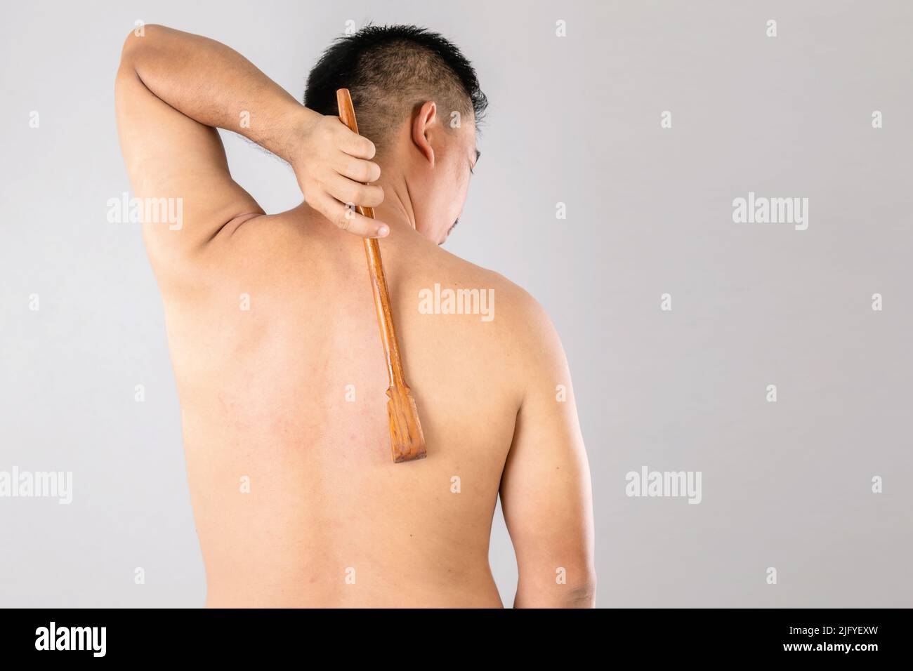 Health Care oder Juckreiz oder Tinea cruris Konzept : Porträt von Menschen mit Scratch Holz Stick Kratzen auf seiner Rückseite. Studio auf grauem Backgro gedreht Stockfoto