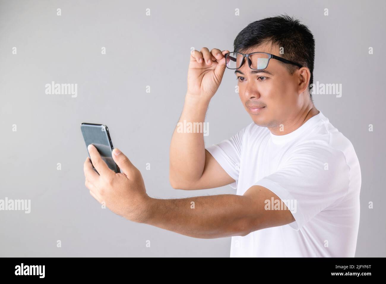 Kurz- oder Weitblick Konzept : Mann wering Brillen und versuchen, klar auf dem Smartphone im Studio auf grauem Hintergrund aufgenommen aussehen Stockfoto