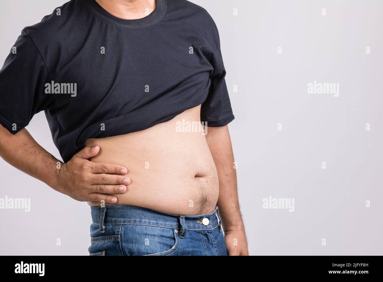 Körperschmerzen, Hüftschmerzen oder Auswirkungen von Leberproblemen : fetter Mann mit der Hand und Druck auf die Hüftposition. Studio auf grauem Hintergrund aufgenommen. Stockfoto