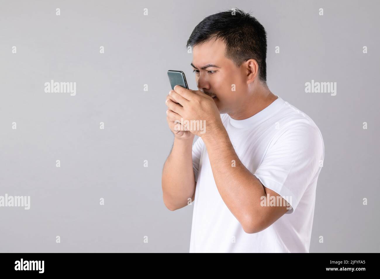 Kurz- oder Weitblick Konzept : Mann versucht, näher auf dem Smartphone im Studio auf grauem Hintergrund aufgenommen zu suchen Stockfoto
