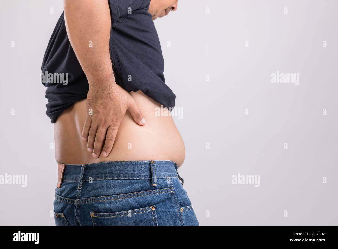 Körperschmerzen, Hüftschmerzen oder Auswirkungen von Leberproblemen : fetter Mann mit der Hand und Druck auf die Hüftposition. Studio auf grauem Hintergrund aufgenommen. Stockfoto