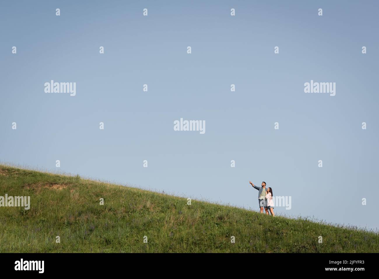 Blick aus der Ferne auf den Mann, der die Frau umarmt und mit dem Finger auf die grüne Wiese zeigt Stockfoto