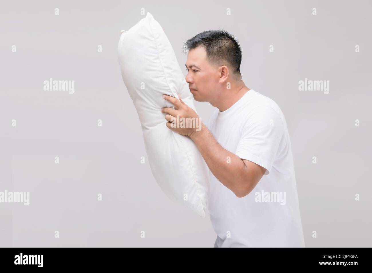 Das Kissen riecht schlecht. Portrait asiatischer Mann mit weißem Kissen und schlechtem Geruch. Studio auf grauem Hintergrund aufgenommen Stockfoto