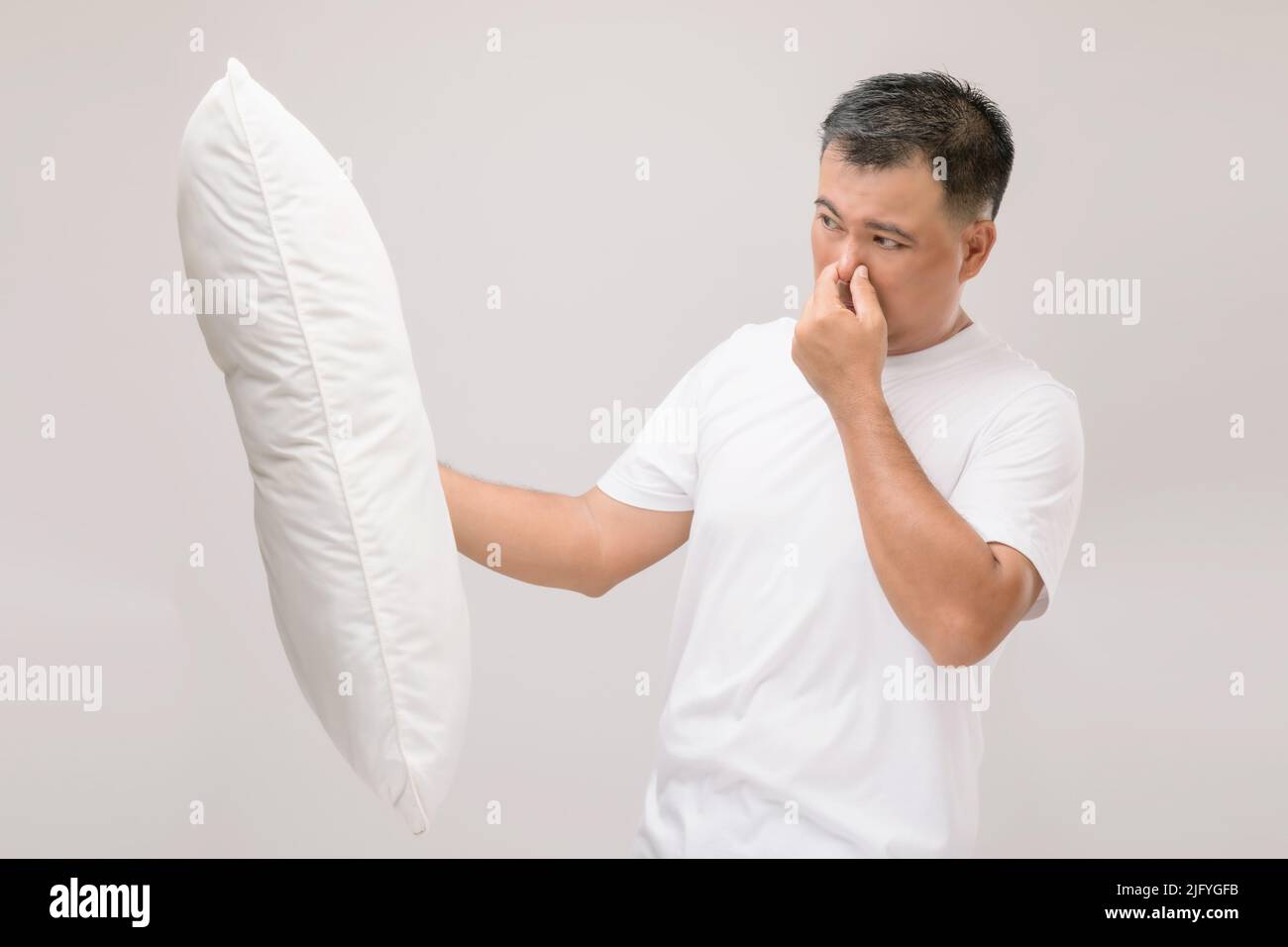 Das Kissen riecht schlecht. Portrait asiatischer Mann mit weißem Kissen und schlechtem Geruch. Studio auf grauem Hintergrund aufgenommen Stockfoto