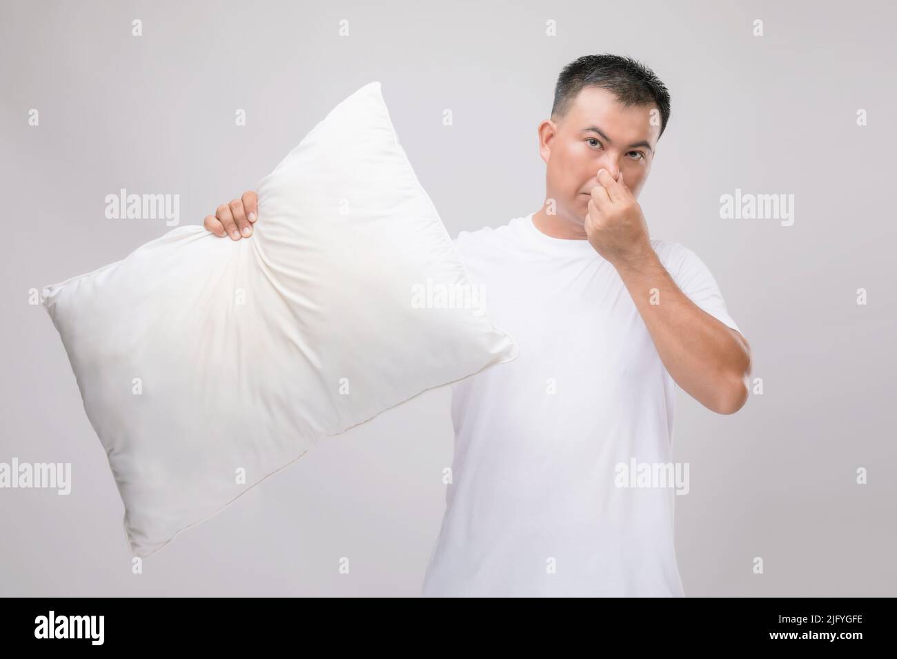 Das Kissen riecht schlecht. Portrait asiatischer Mann mit weißem Kissen und schlechtem Geruch. Studio auf grauem Hintergrund aufgenommen Stockfoto