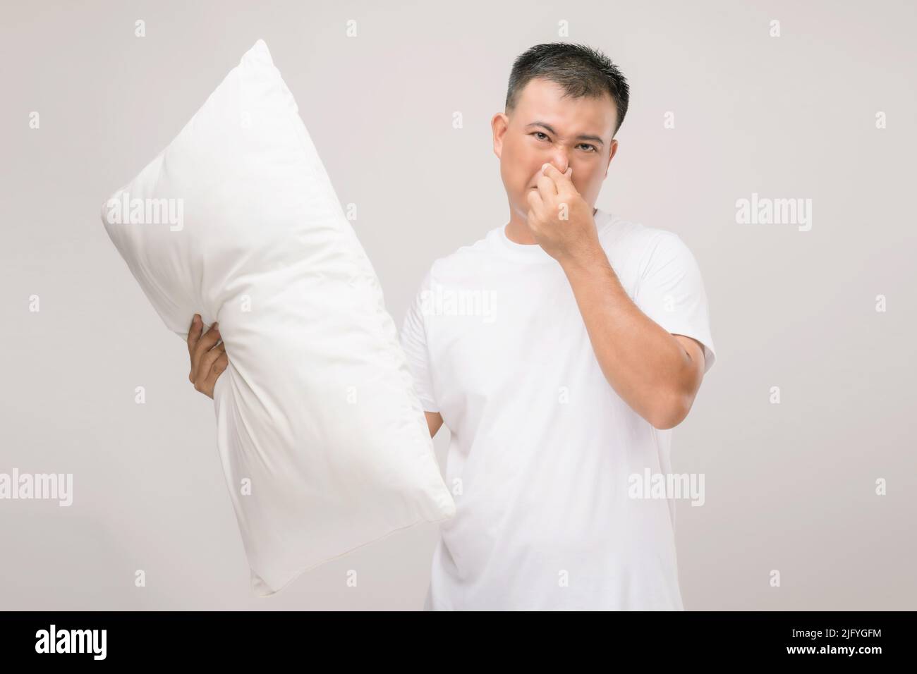 Das Kissen riecht schlecht. Portrait asiatischer Mann mit weißem Kissen und schlechtem Geruch. Studio auf grauem Hintergrund aufgenommen Stockfoto