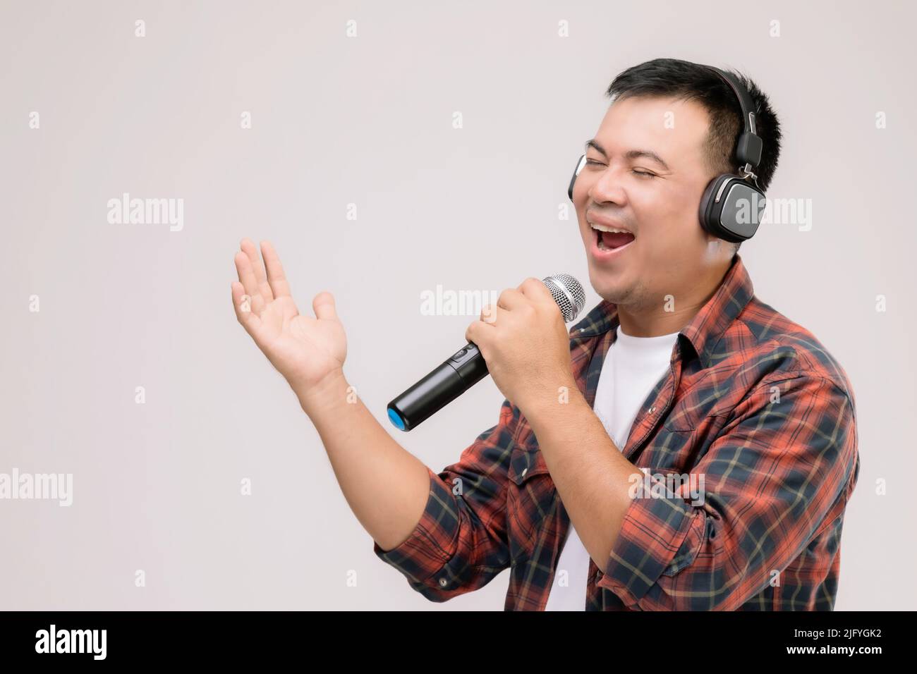 Ein Mann aus dem asiatischen Hochformat hört Lieder oder Musik von einem schwarzen Kopfhörer. Studioaufnahme isoliert auf grauem Hintergrund Stockfoto