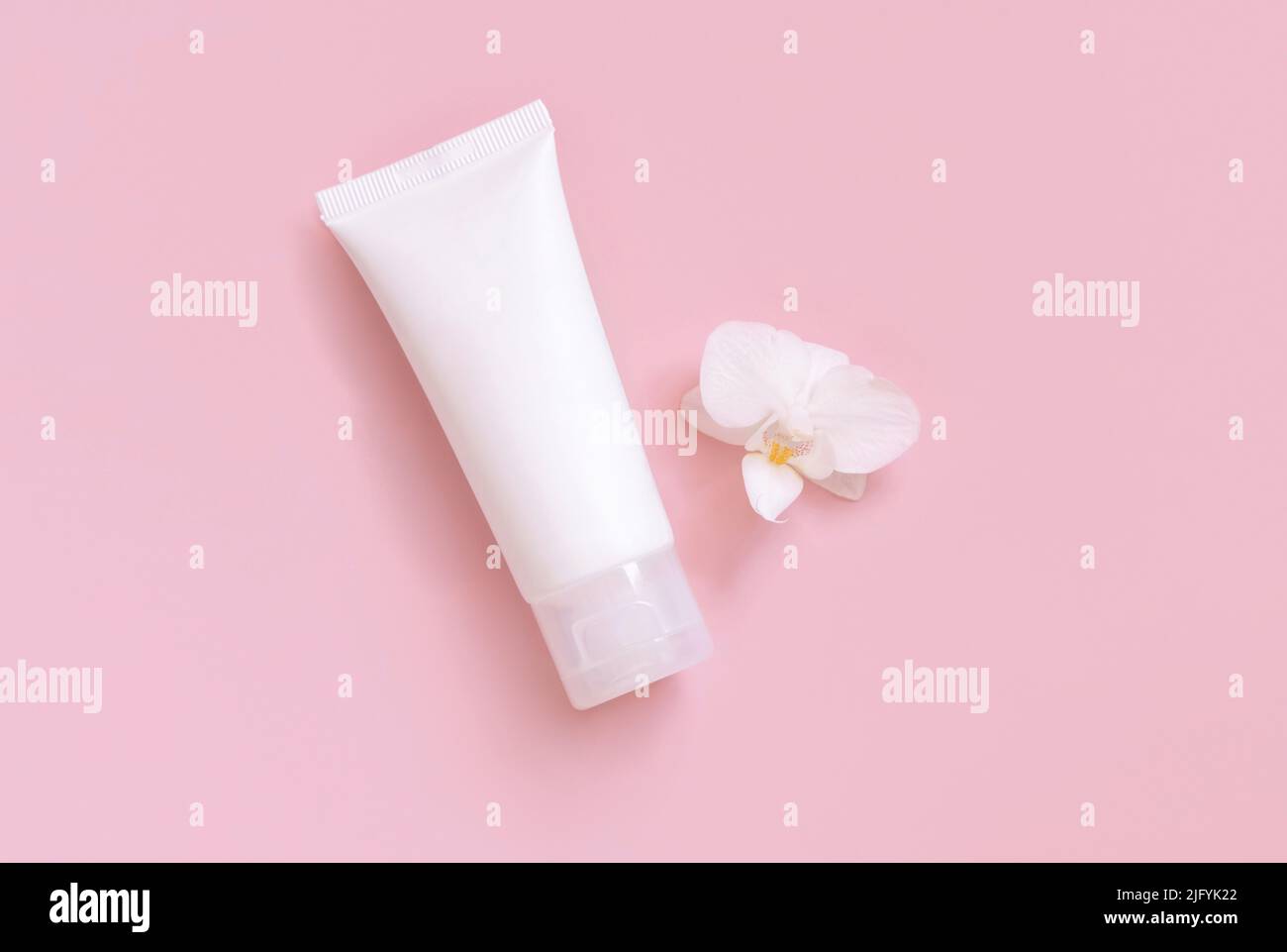 Weiße Plastik-cremefarbene Röhre in der Nähe der weißen Orchideenblume auf hellgelb, Draufsicht, Mockup. Hautpflegeprodukt, Creme oder Lotion. Exotische Naturkosmetik Stockfoto