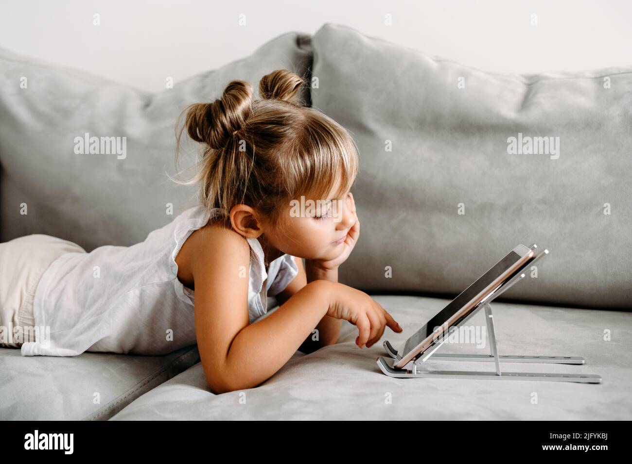 Kleinkind Mädchen liegt auf der Couch zu Hause und spielt mit digitalen drahtlosen Tablet-Computer. Baby Kind wächst mit Online-Anwendungen. Stockfoto