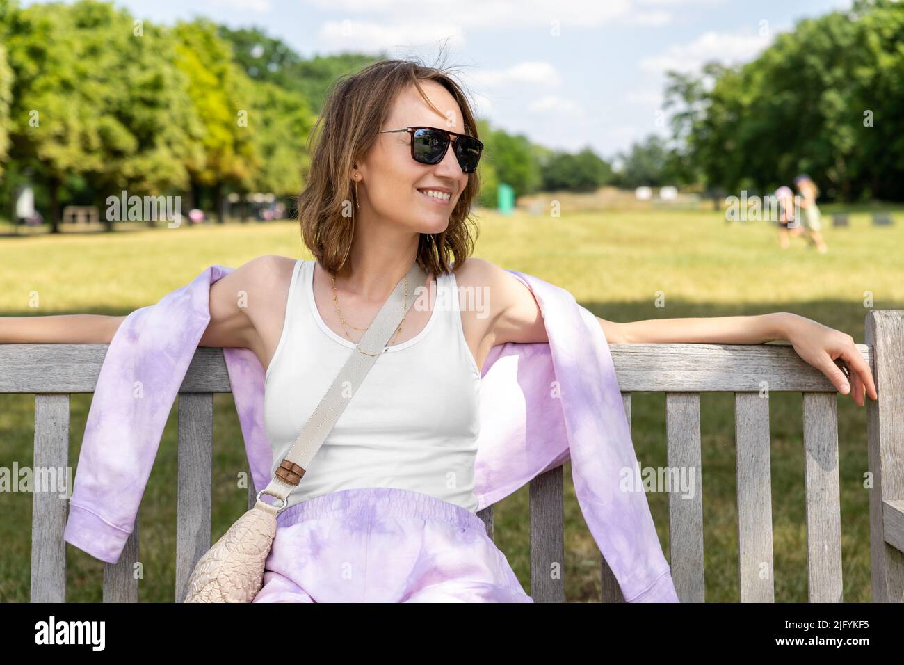 Porträt junger Erwachsener Attraktive Frau genießt es, auf der Bank zu sitzen und entspannt zu entspannen, unbeschwerte Ruhe im Stadtpark vor grünem Gras und Bäumen an sonnigen Tagen Stockfoto