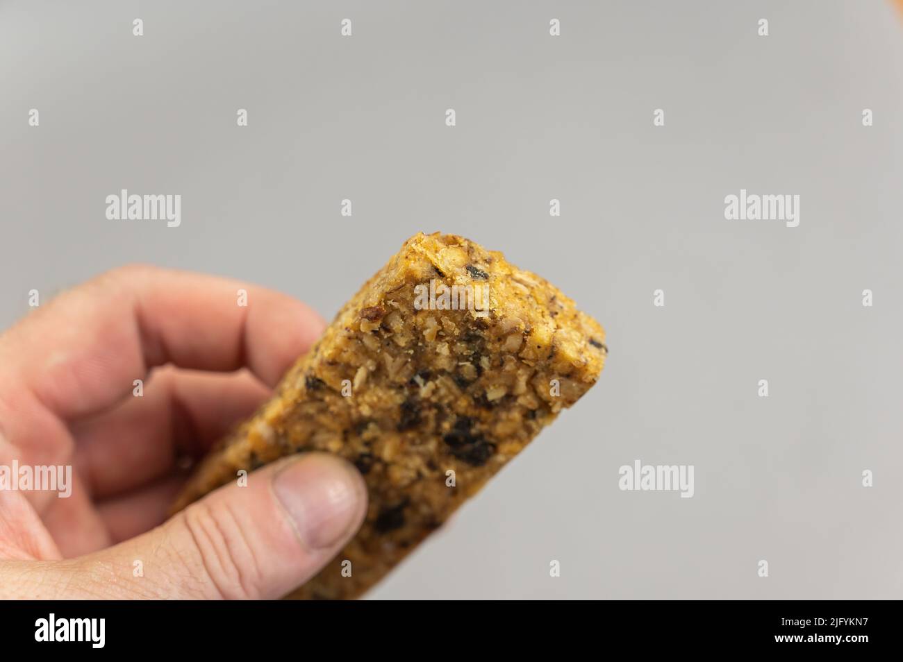 Ein Mann hält Protein Energy Bar in der Hand auf Braun. Ein glutenfreier, zuckerfreier Snack. Haferflocken mit Obst. Gesunde Lebensmittel. Stockfoto