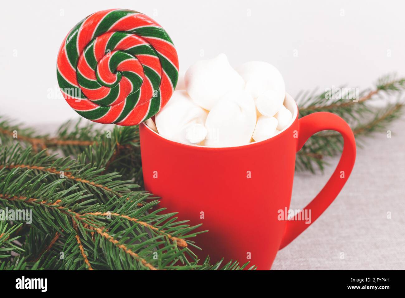 Roter Becher voller Weihnachtsleckereien, umgeben von grünen Tannenzweigen. Stockfoto