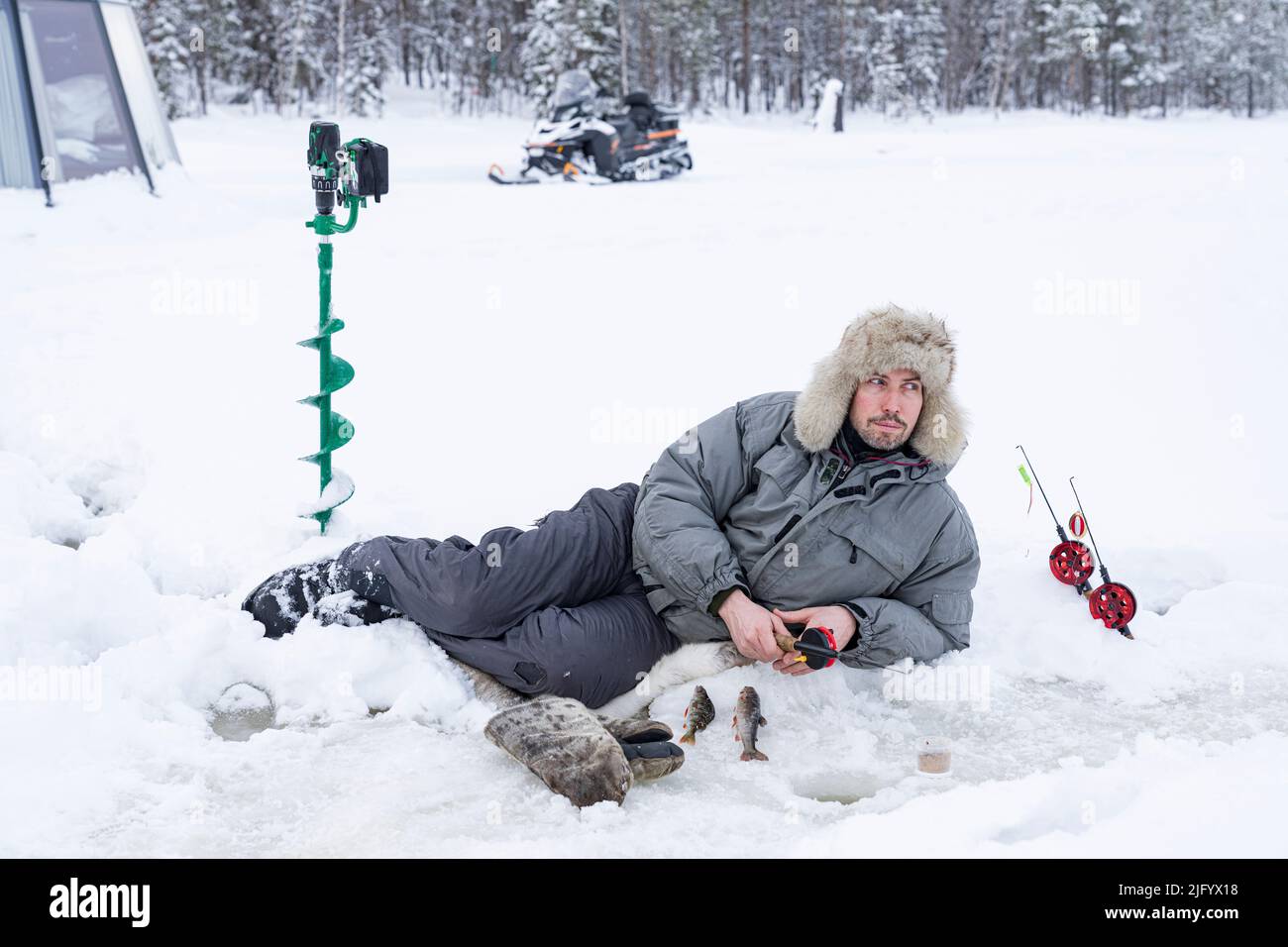Mann, der auf Eis liegt, während er aus einem Loch fischt, Lappland, Schweden, Skandinavien, Europa Stockfoto