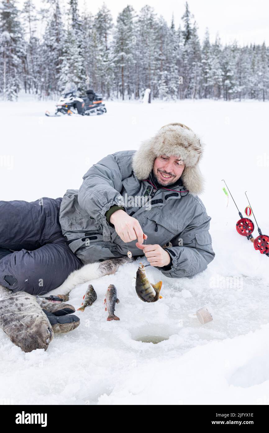 Fröhlicher Mann, der den Fischfang aus dem Eisloch, Lappland, Schweden, Skandinavien und Europa auffängt Stockfoto