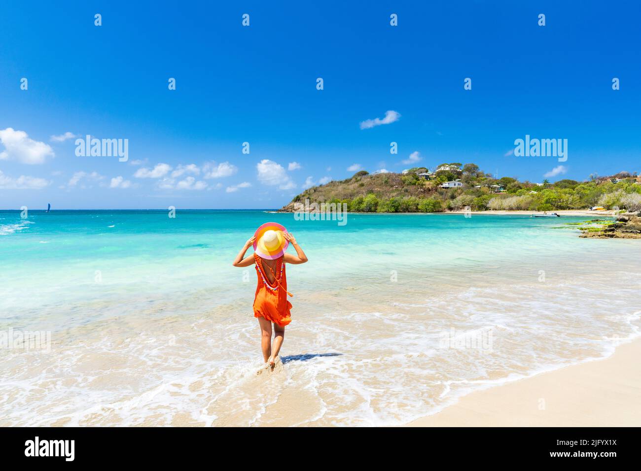 Schöne Frau mit orangefarbenem Kleid und Strohhut, die an einem tropischen Strand, Antigua, Westindien, Karibik, Mittelamerika steht Stockfoto