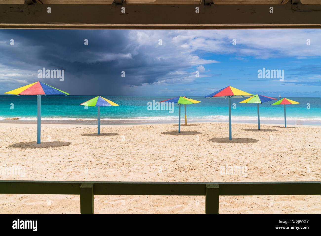 Bunt gestreifte Sonnenschirme am weißen Sandstrand unter Sturmwolken, Antigua, Westindien, Karibik, Mittelamerika Stockfoto