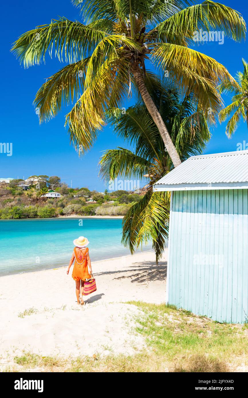 Tourist in orangefarbenem Kleid zu Fuß am palmengesäumten Strand, Antigua, Leeward Islands, Westindien, Karibik, Mittelamerika Stockfoto
