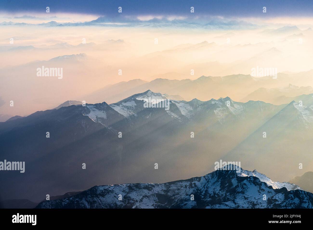 Fliegen Sie über die schneebedeckten Gipfel der Lepontine und der Tessiner Alpen, die bei Sonnenuntergang von Sonnenstrahlen am romantischen Himmel erleuchtet sind, Schweiz, Europa Stockfoto