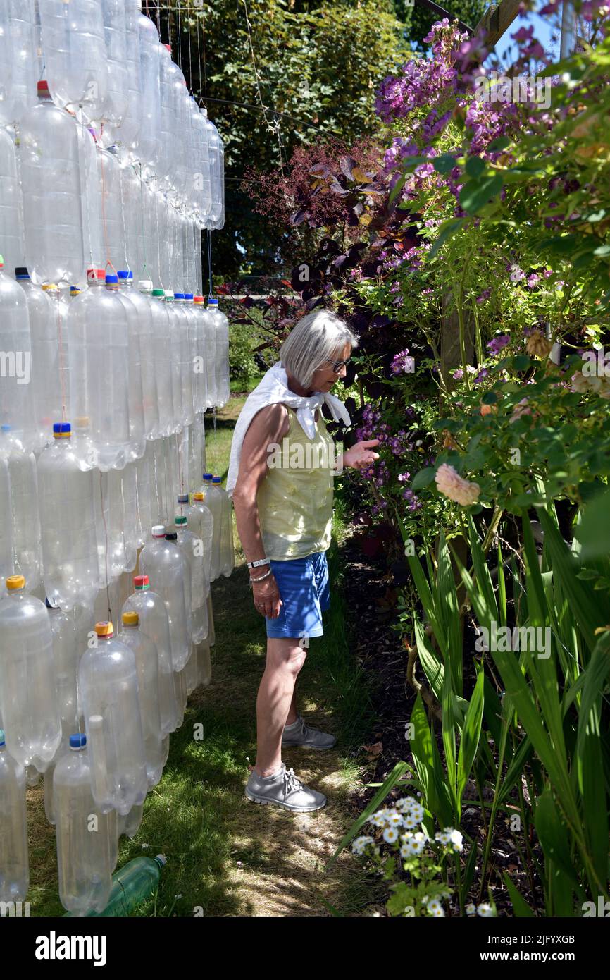 Ältere Frau im Rosengarten mit Kunstausstellung aus Plastikflaschen Stockfoto