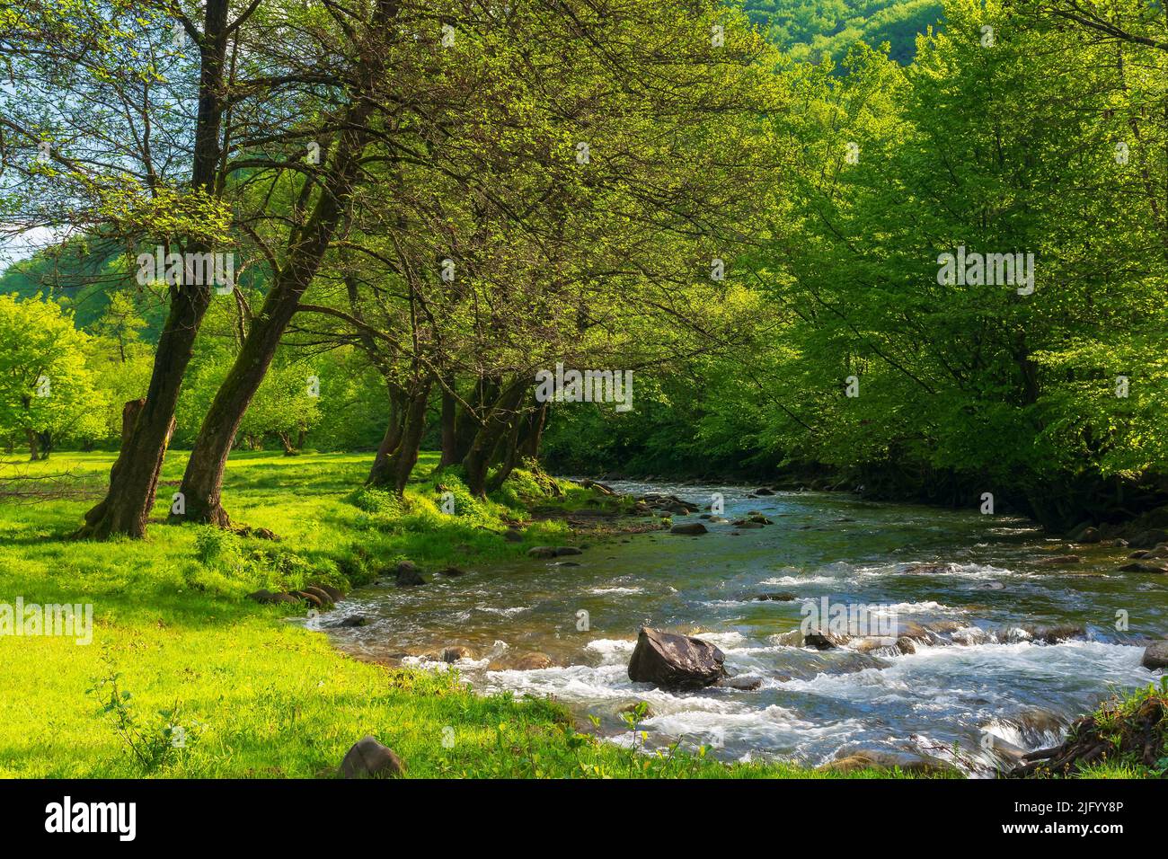 Frühlingslandschaft mit Fluss zwischen Park. Berge in der Ferne. Sonniger Tag und blauer Himmel mit Wolken Stockfoto