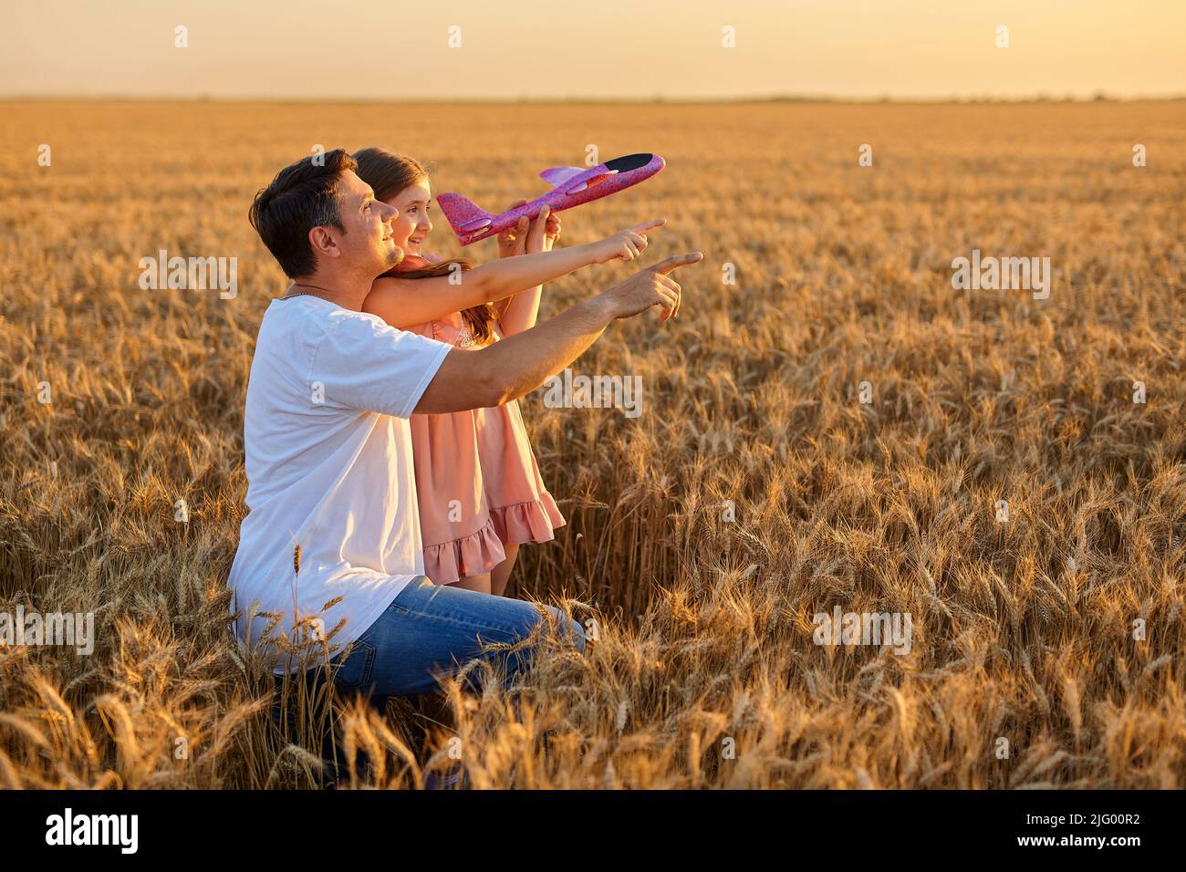 Nettes Mädchen spielt mit Spielzeug Flugzeug gegen Himmel im Weizenfeld Stockfoto