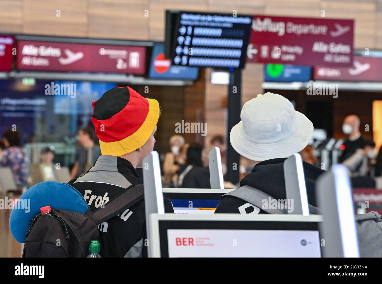 06. Juli 2022, Brandenburg, Schönefeld: Reisende warten beim Check-in ...