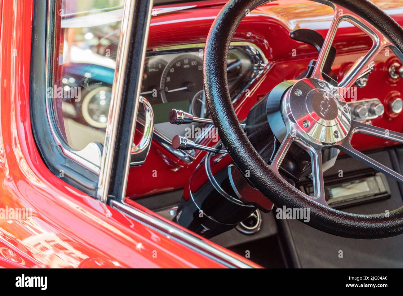 Andover, MA, USA, 26. Juni 2022: Nahaufnahme des Lenkrads in einem leuchtend roten Chevrolet-Oldtimer der Ära 1950s - 1960s. Stockfoto