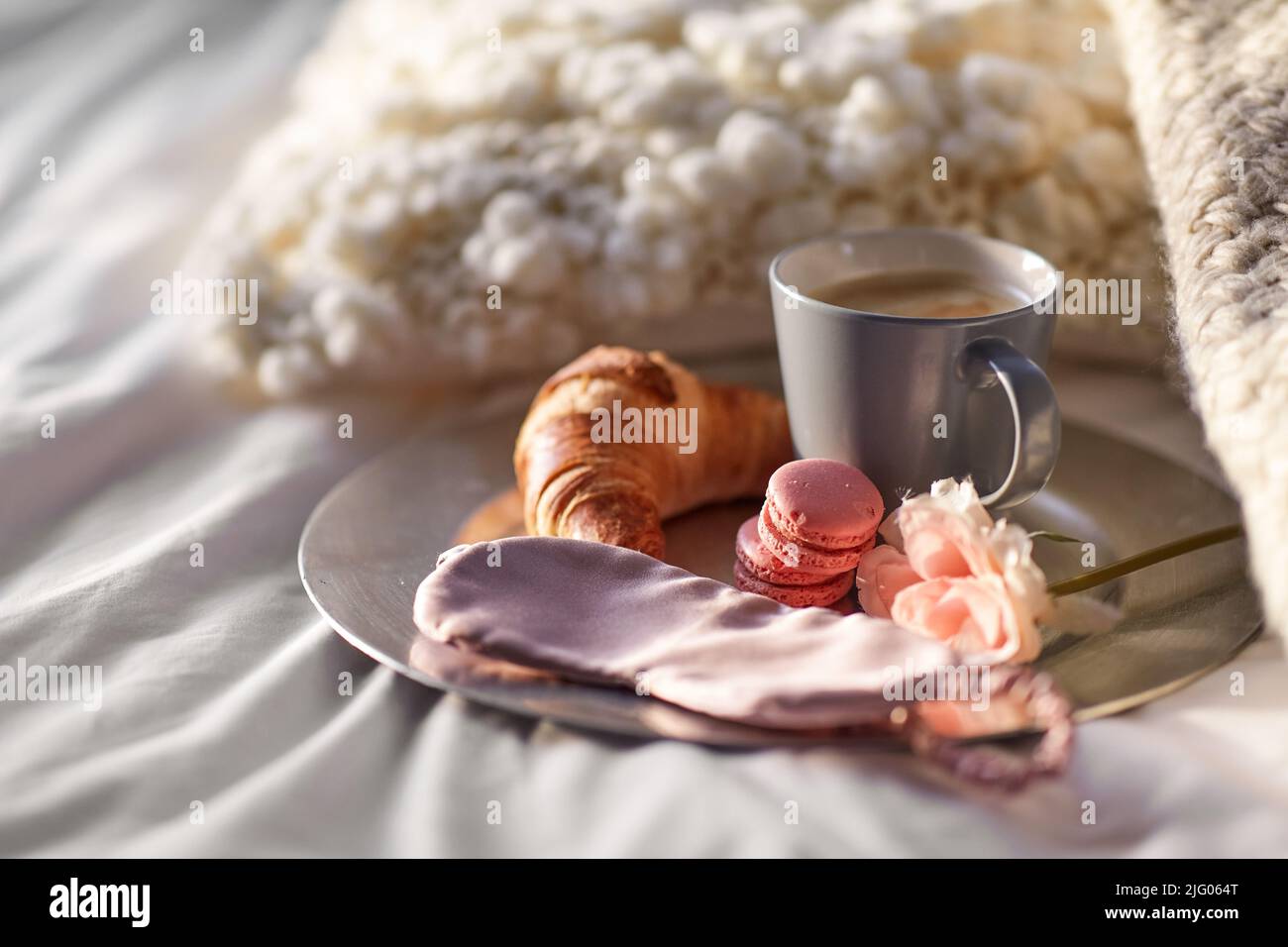 Croissant, Kaffee und Augenmaske im Bett Stockfoto