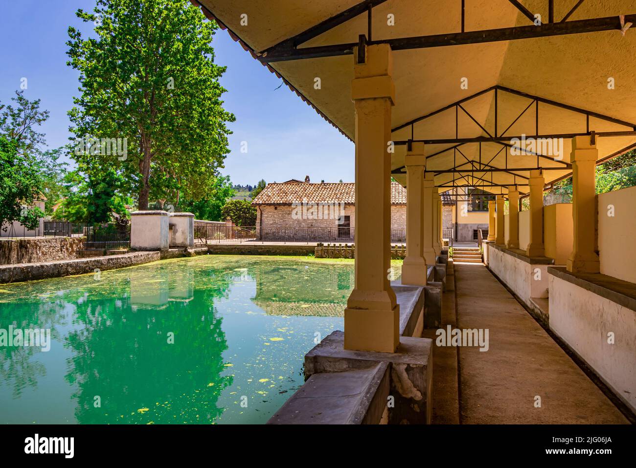 Das alte Waschhaus, am Fluss, im mittelalterlichen Dorf Bevagna. Umbrien, Italien, Perugia. Der blaue Himmel, Bäume und Vegetation. Grünalgen auf t Stockfoto