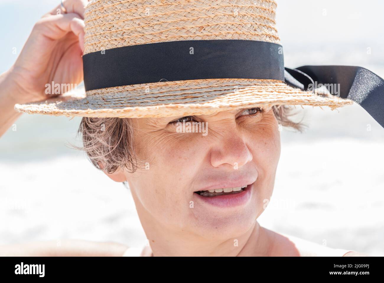 Nahaufnahme eines Porträts einer verheirateten grauhaarigen Frau, die ein wenig lächelt und etwas am Strand beobachtet. Urlaubskonzept. Stockfoto