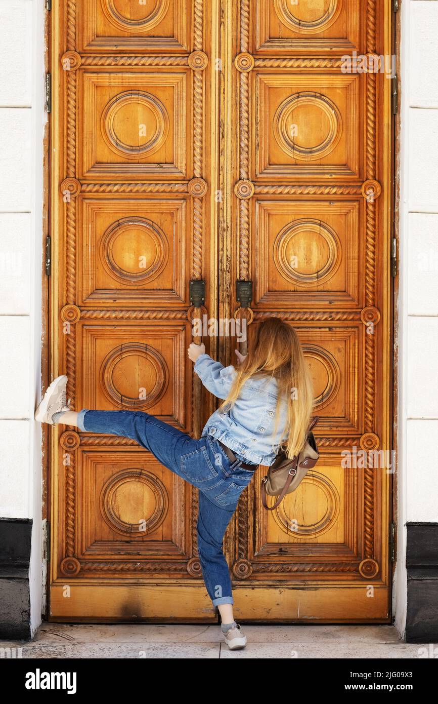 Eine Frau versucht, massive Holztüren mit klassischem Muster gewaltsam zu öffnen. Brechen Sie in eine verschlossene Tür ein. Stockfoto