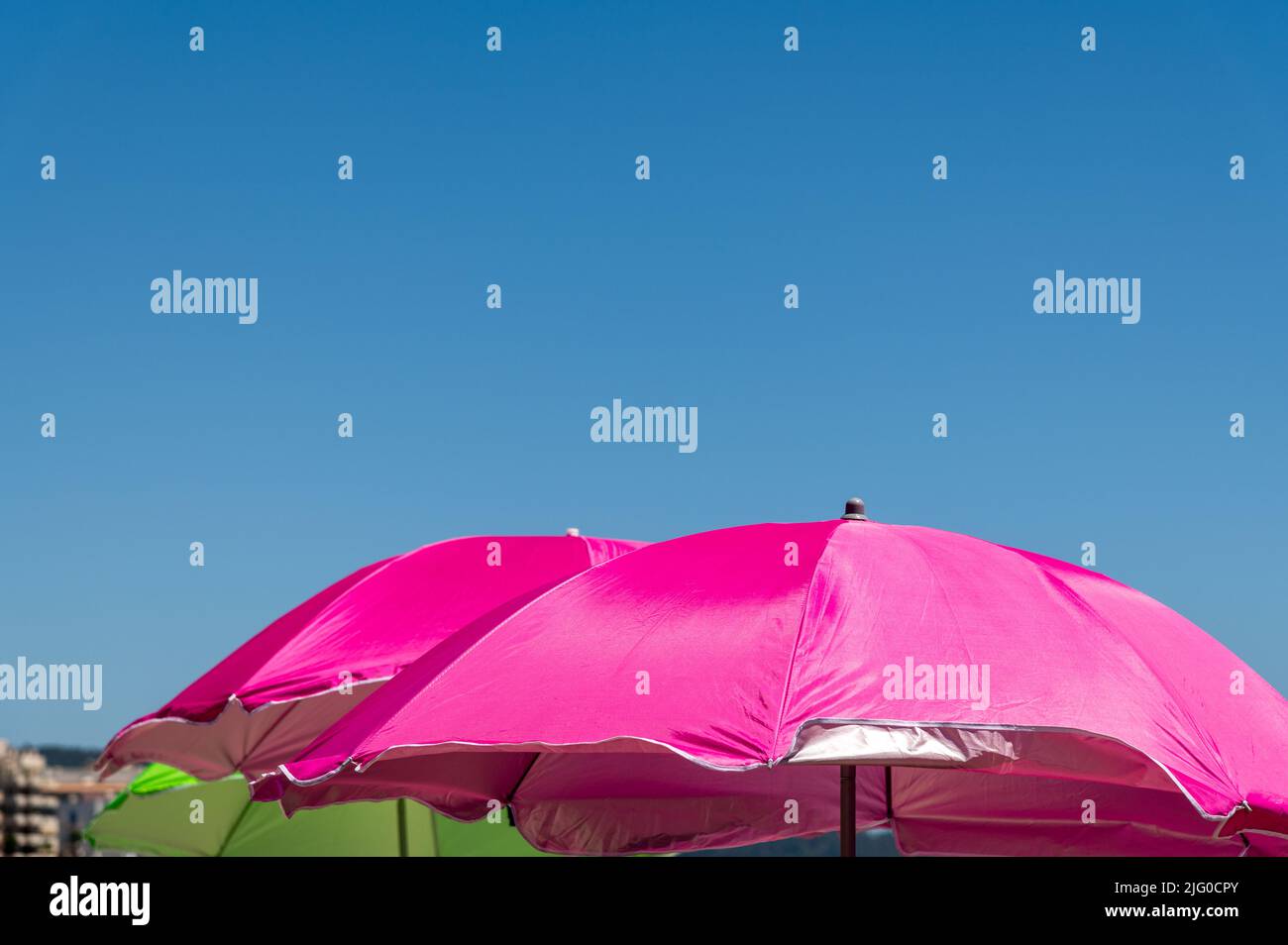 Farbenfrohe rosa und grüne Sonnenschirme vor dem klaren blauen Himmel Stockfoto