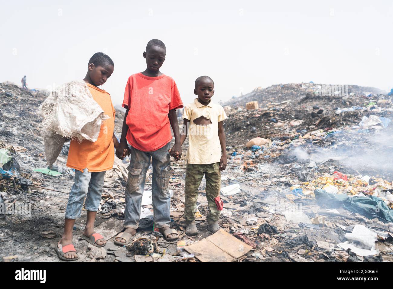 Drei elende afrikanische Streetboys verdienen ihren Lebensunterhalt, indem sie Metalle, Plastik und andere Materialien aus einer schmutzigen und rauchenden Deponie recyceln Stockfoto