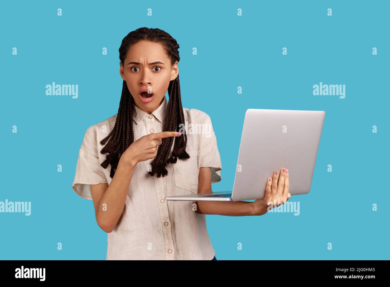 Erstaunt Frau schockiert operativen Software-Probleme, zeigt auf Laptop-Bildschirm, afraids des Datenverlustes, trägt weißes Hemd. Innenaufnahme des Studios isoliert auf blauem Hintergrund. Stockfoto