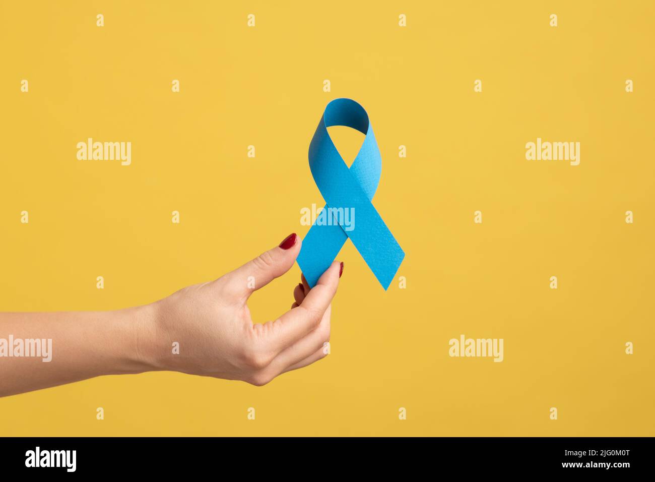 Nahaufnahme der Frau Hand mit Maniküre hält blaues Band, Symbol der männlichen Gesundheit, Prostatakrebs Bewusstsein, Frieden und genetische Störung. Innenaufnahme des Studios isoliert auf gelbem Hintergrund. Stockfoto