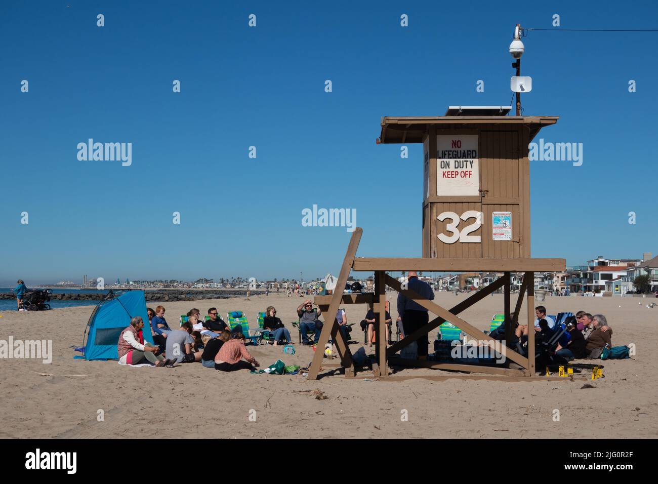 Gruppe von Menschen, die bei einem Treffen neben einer Rettungsschwimmerhütte am Strand zuhören. In Newport Beach, Südkalifornien, USA Stockfoto