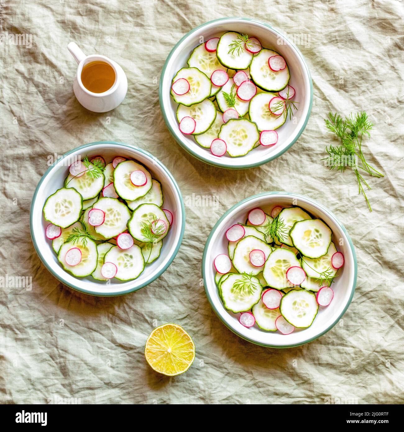 Drei kleine runde Schüsseln mit Rettich und Gurke Sommer Licht Salat, grüner Textil-Hintergrund, Draufsicht Stockfoto