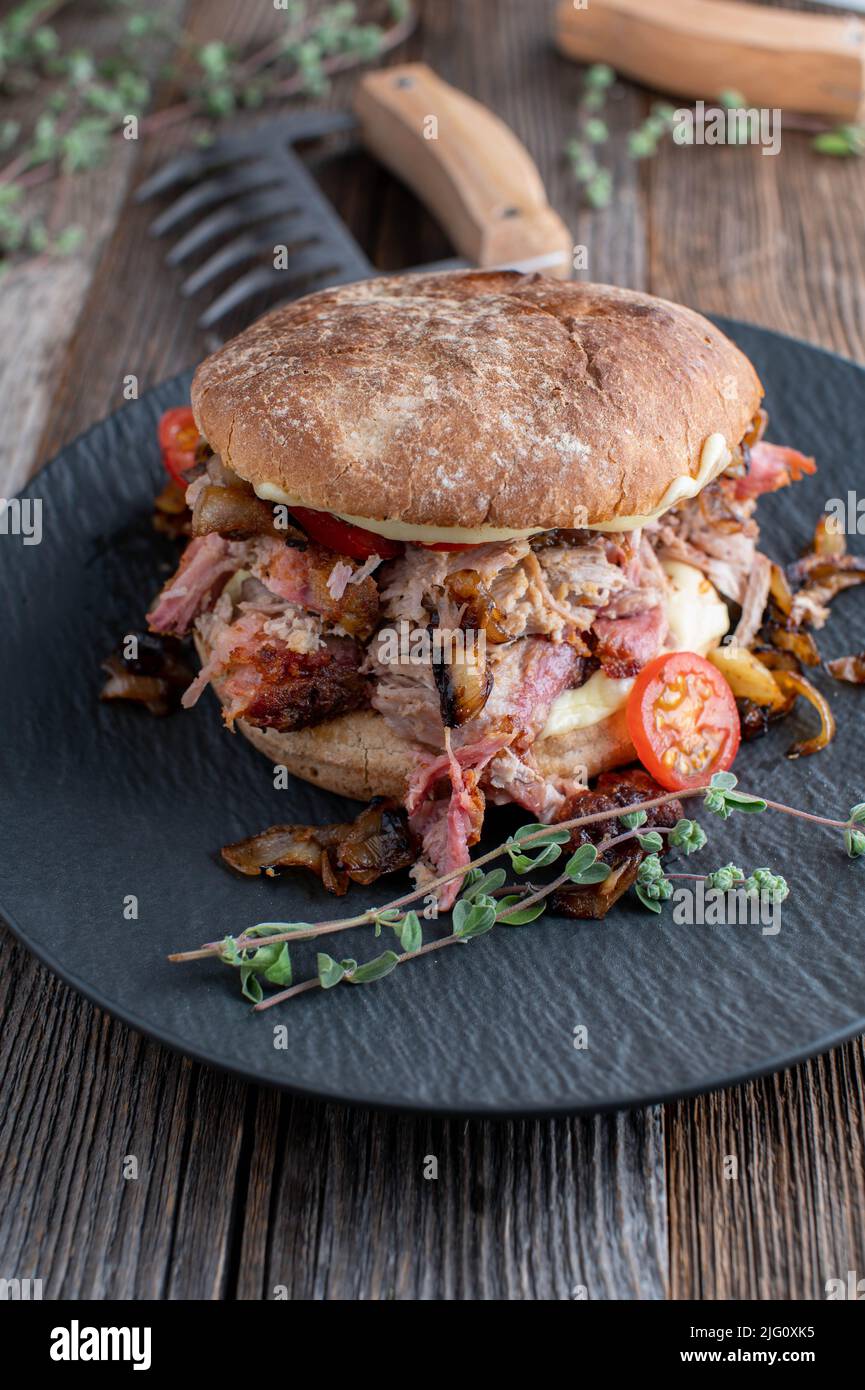 Burger mit Schweinefleisch, Käse, Tomaten und gebratenen Zwiebeln auf Holztisch Stockfoto