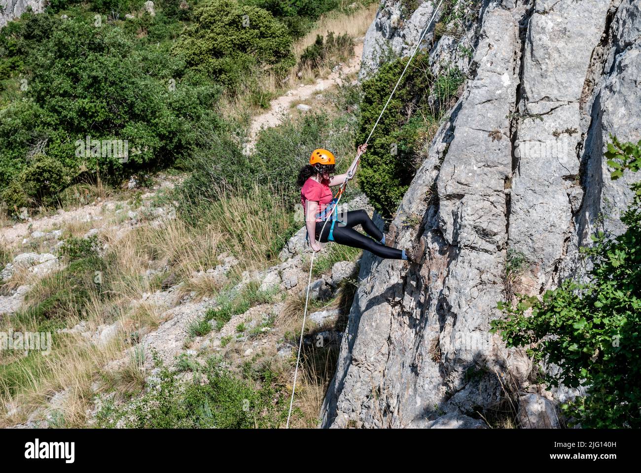 Schöne Frau klettert auf hohen Felsen bei Sonnenuntergang Nebel in den Bergen. Konzept von Abenteuer und Extremsport Stockfoto