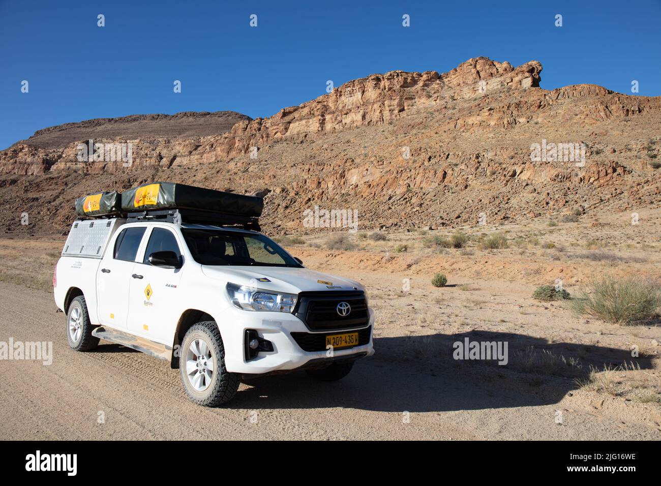 Fahrzeug mit Allradantrieb auf einer abgelegenen Wüstenstraße in Namibia, mit felsigen Hügeln im Hintergrund. Stockfoto