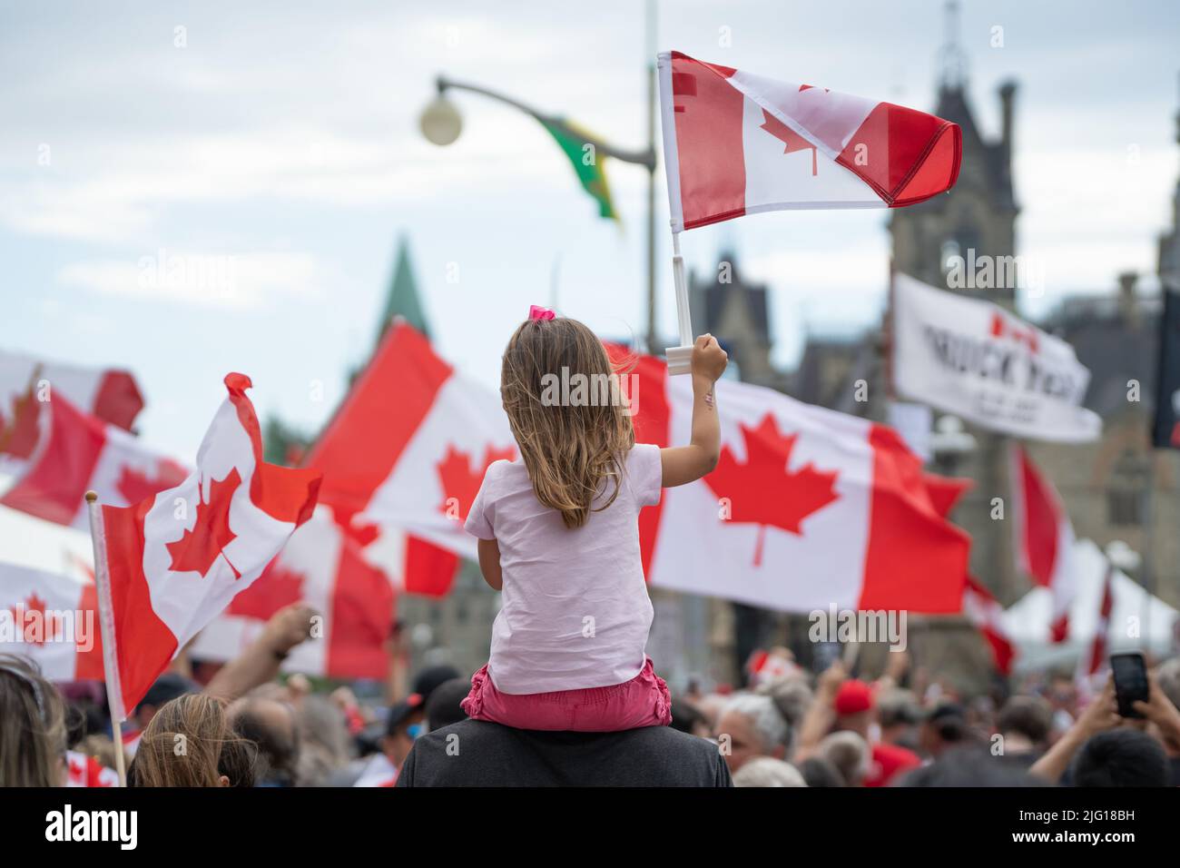 Ein junges Mädchen hält eine Kanada-Flagge hoch, während sie auf dem Rücken ihres Vaters während einer Freiheitskundgebung am Canada Day auf dem Parliament Hill in Ottawa sitzt. Stockfoto