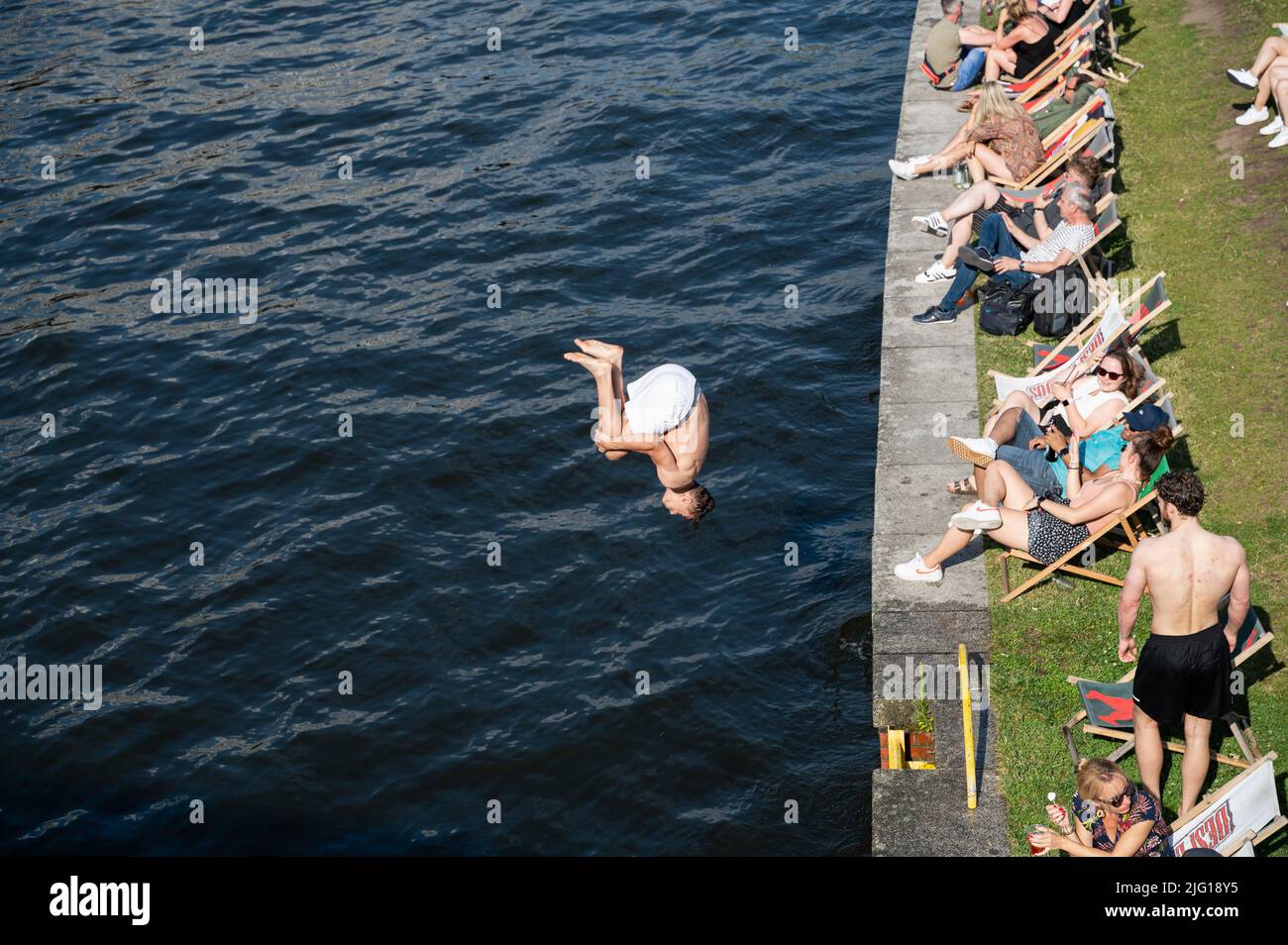 03.07.2022, Berlin, Deutschland, Europa - Ein junger Mann springt mit einem Backflip vom Spreeufer neben einer Strandbar ins kühle Nass. Stockfoto