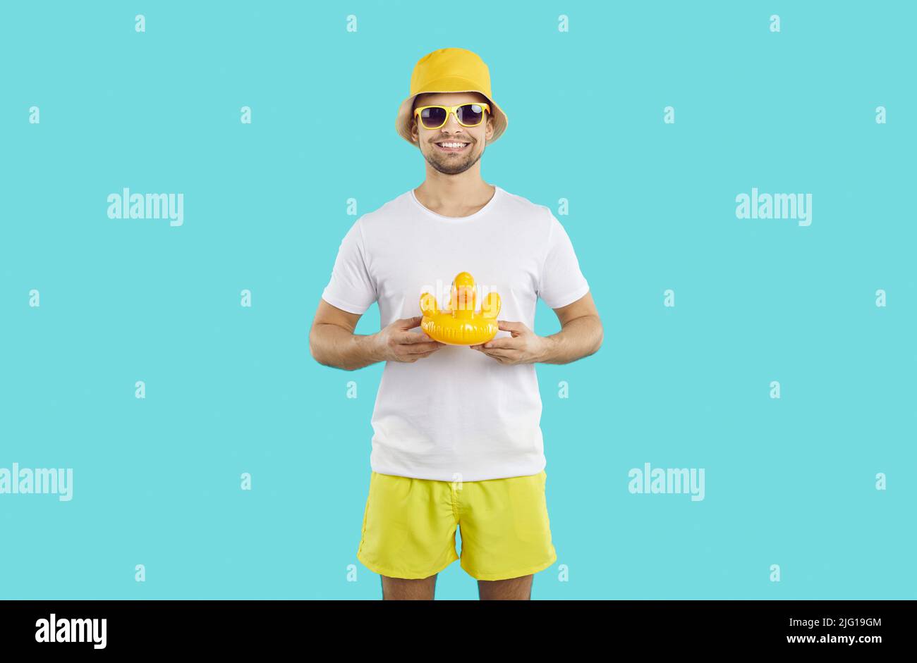 Ein junger, positiver Kaukasusmann mit Sonnenbrille hält die gelbe Ente für Schwimmstände im Studio Stockfoto