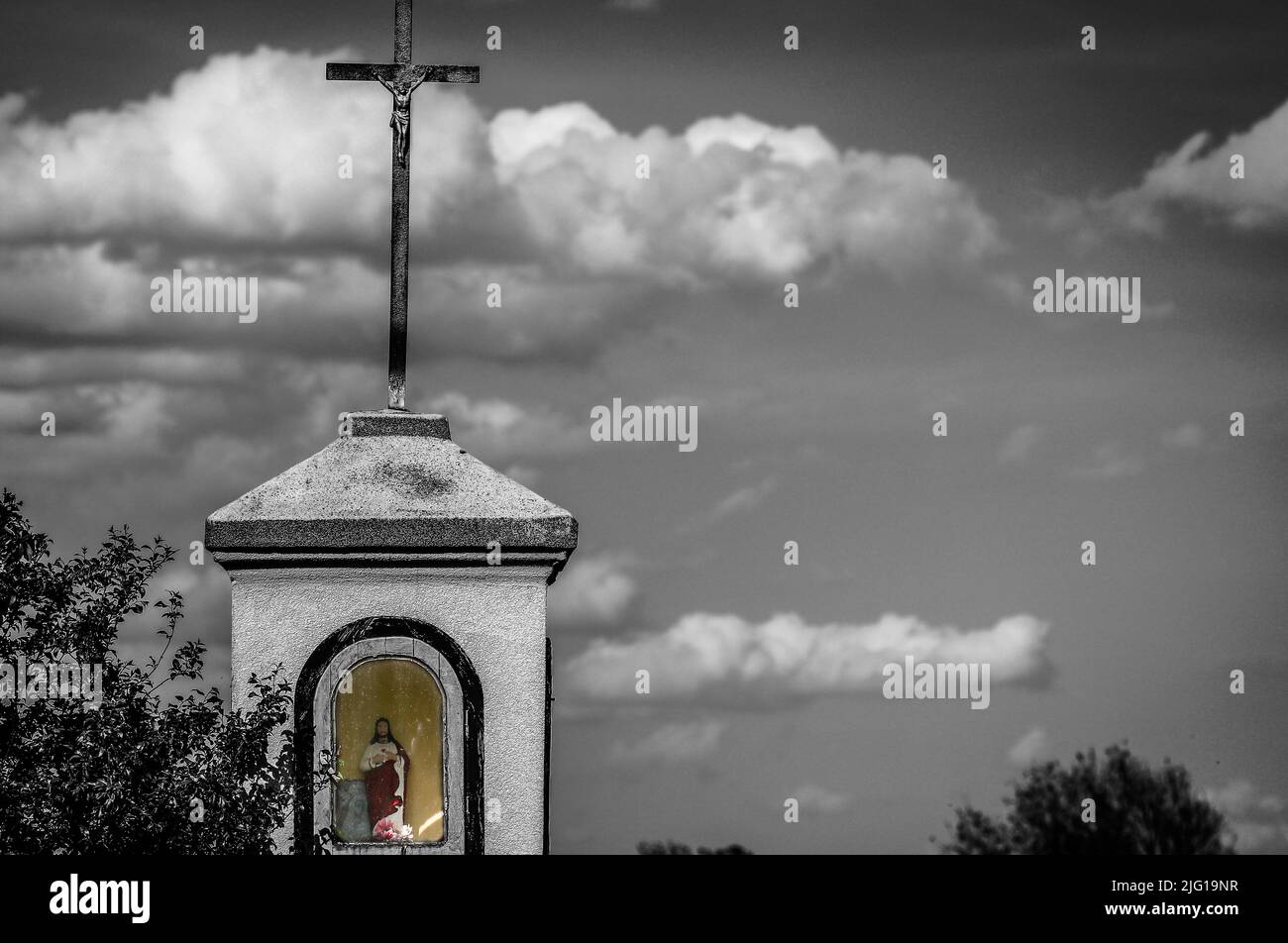 Alter Schrein auf dem Weg in polnischer Landschaft gegen bewölkten Himmel mit Kopierraum, monochromes Bild mit ausgewählter Farbe Stockfoto