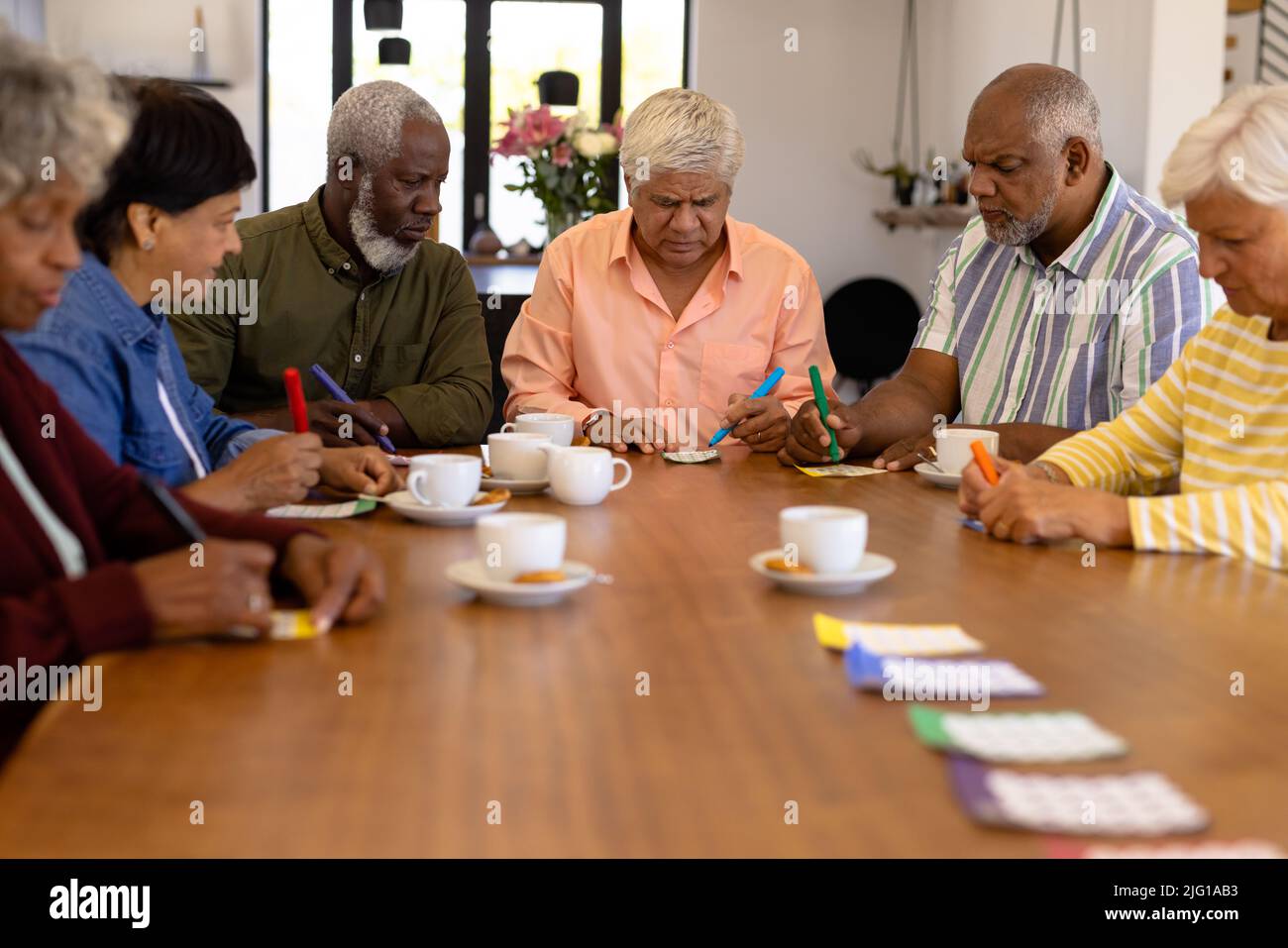 Mehrrassige ältere männliche und weibliche Freunde mit Kaffee und Keksen auf dem Esstisch, die Bingo spielen Stockfoto