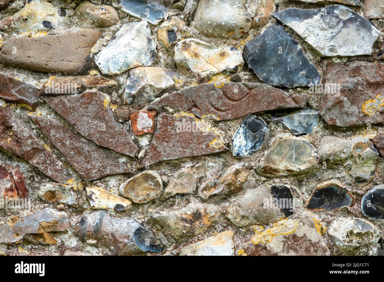 Flushwork Feuerstein Kirchenwand gefüllt mit Fragmenten von eingravierten gebrochenen Fußsteinen in rotem Sandstein Stockfoto
