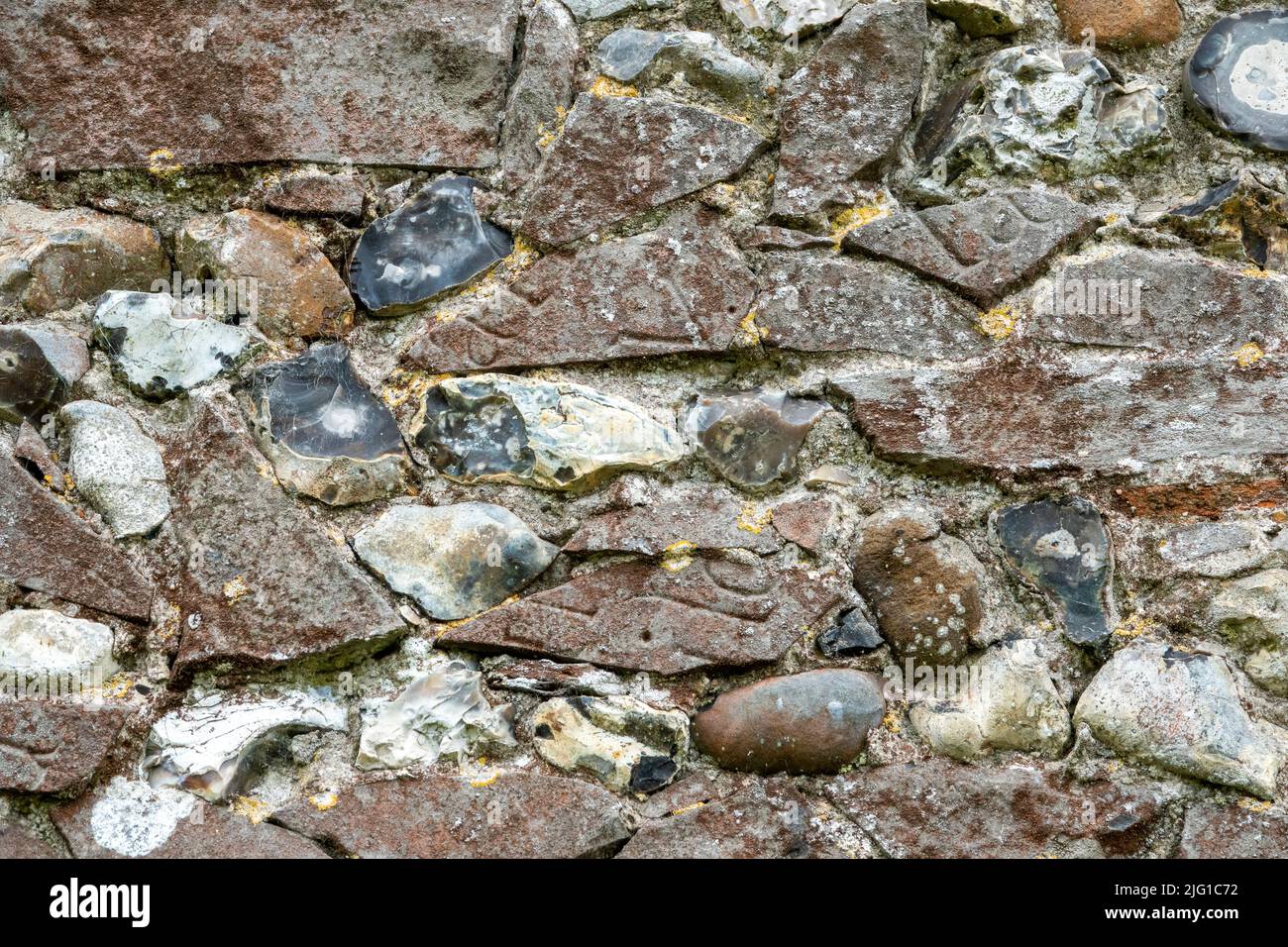 Flushwork Feuerstein Kirchenwand gefüllt mit Fragmenten von eingravierten gebrochenen Fußsteinen in rotem Sandstein Stockfoto