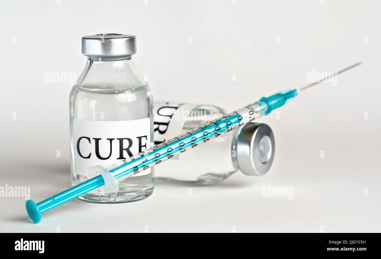 Glas-Impffläschchen mit Etikett Cure auf weißem Brett, blaugrüne Unterspritze nahe - Impfkonzept Stockfoto